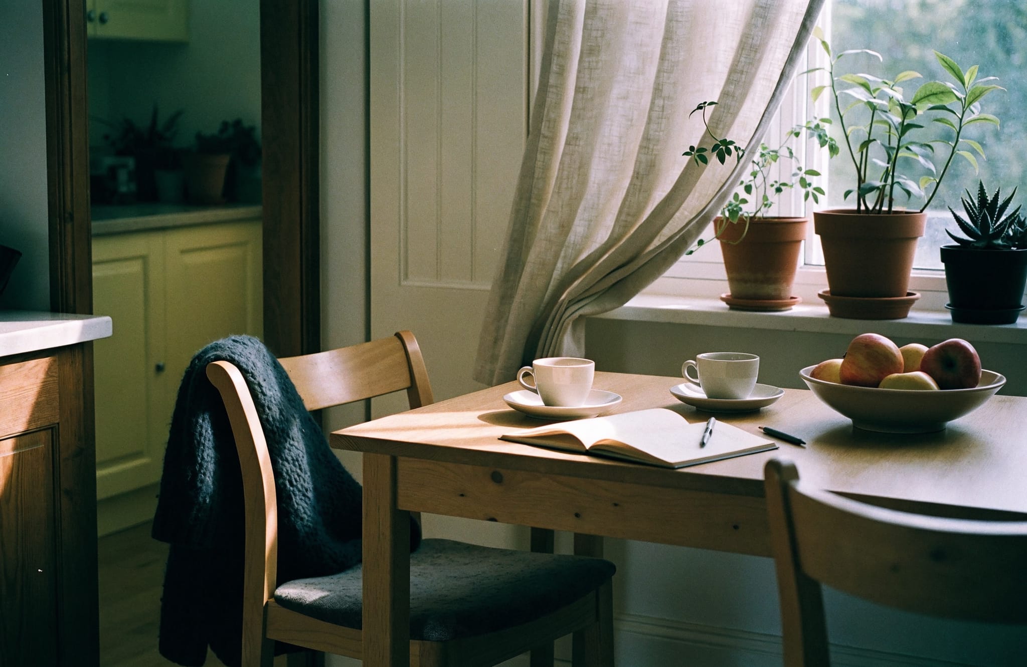 Ett köksbord vid ett fönster med två kaffekoppar och ett anteckningsblock.